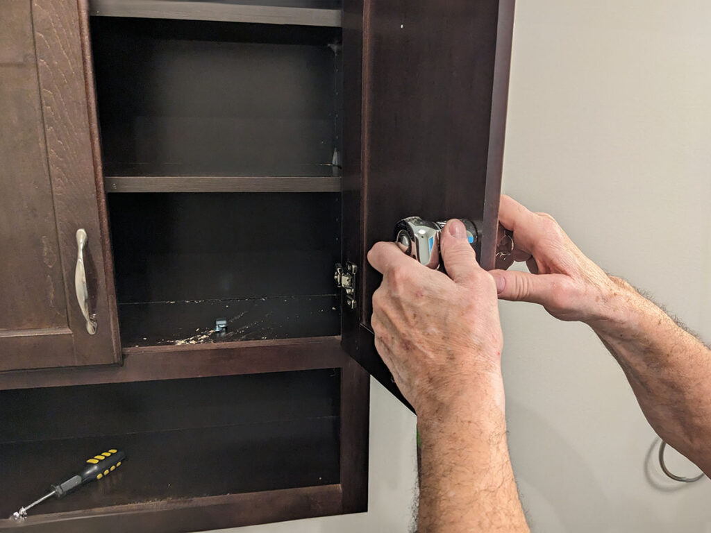 A man is fixing a wall cabinet door handle and lock.