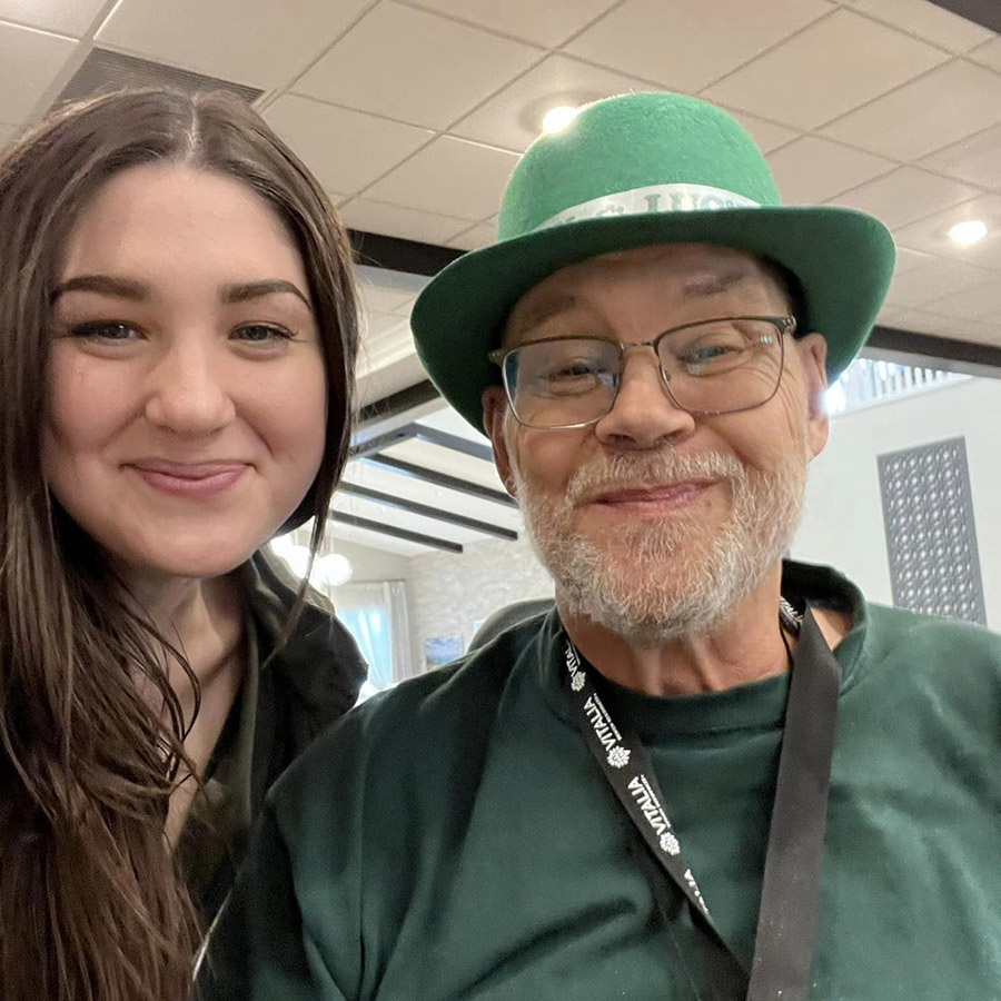 Two people, a senior resident and an employee, smiling in a photo while wearing green for St. Patrick's Day.