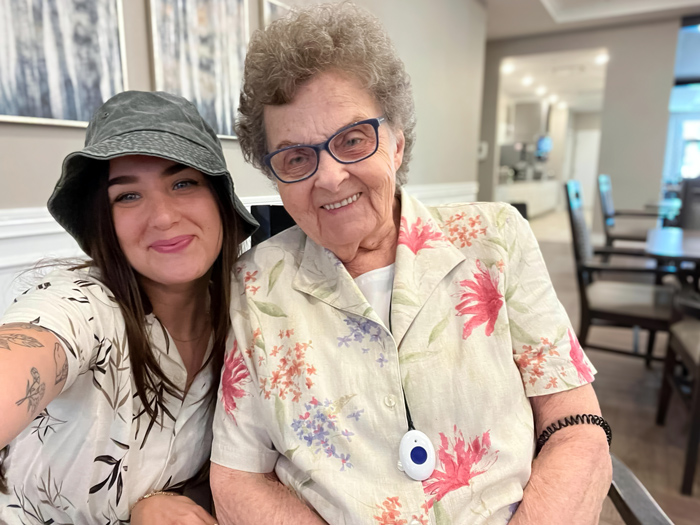 A senior lady and a young woman smile for a selfie together, both wearing floral shirts, creating a joyful and connected moment in a bright indoor setting.