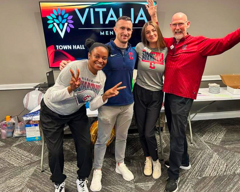 Group photo of team members at Vitalia Mentor celebrating a town hall event, wearing Cleveland Guardians-themed attire with cheerful expressions and lively energy.