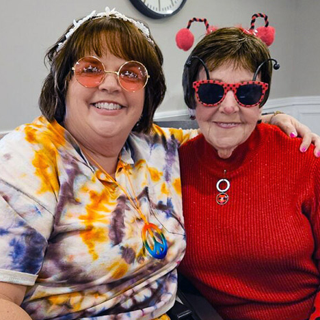 Two women smile beside one another, wearing novelty glasses and antennae for a fun event.