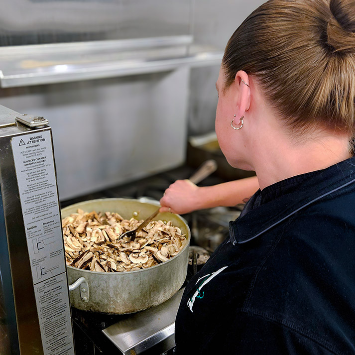 Culinary Team member at Vitalia Mentor stirs a pot full of cooking mushrooms.