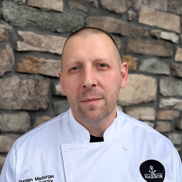 Torsten Marburger, Culinary Director at Vitalia Mentor, posing in a professional headshot, wearing a white chef coat, with a stone wall background.